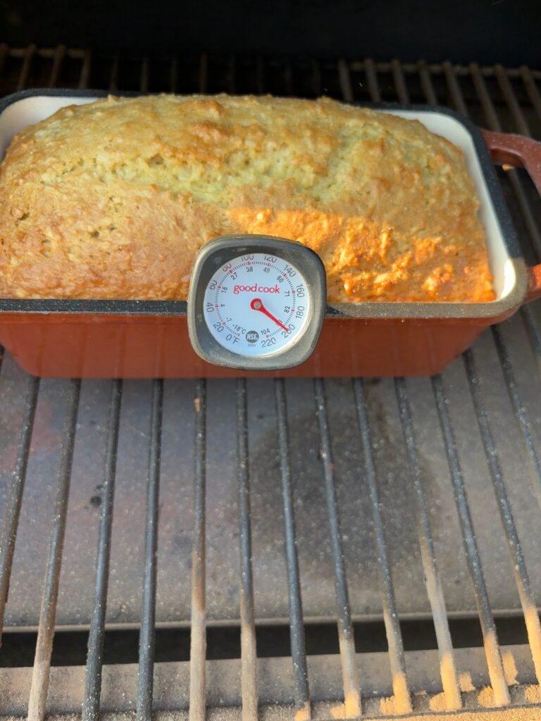Apple nut bread baking on a Traeger grill with an oven thermometer in front of the loaf.